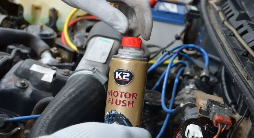 Ręka w rękawiczce trzyma puszkę płukanki do silnika motocyklowego K2 Motor Flush, gotowa do użycia w silniku.