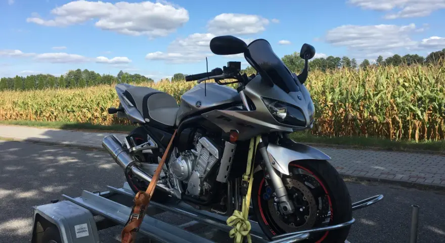 Srebrny motocykl Yamaha na przyczepce, gotowy do rejestracji z Niemiec. W tle pole kukurydzy i błękitne niebo z chmurami.
