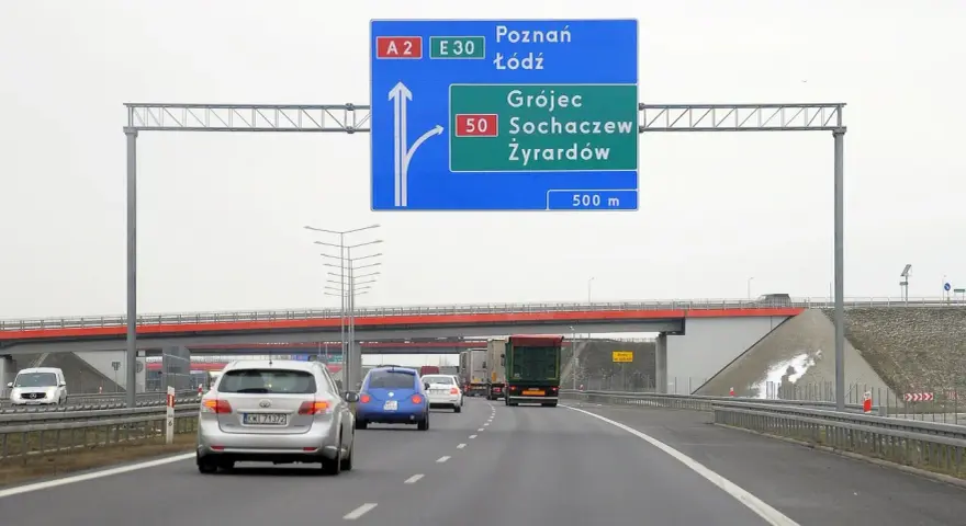 Autostradą A2 w kierunku Poznania i Łodzi. Znak informuje o minimalnej prędkości na autostradzie i zjeździe na Grójec, Sochaczew, Żyrardów za 500 m.