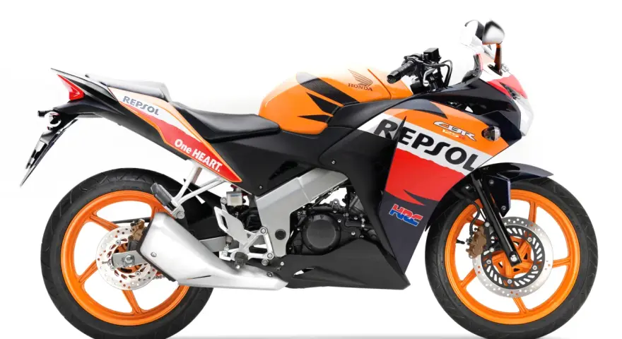 Pomarańczowo-czarny motocykl Honda CBR 125R w barwach Repsol, gotowy do wyścigów.