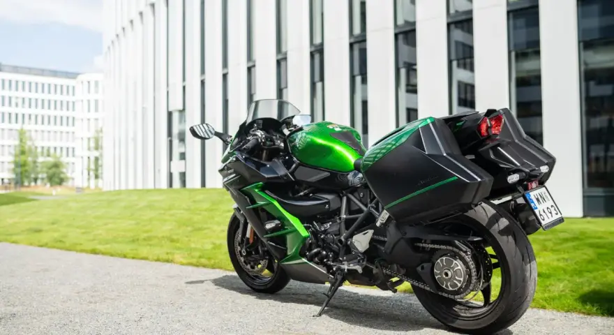Zielony Kawasaki Ninja H2 z czarnymi kuframi, gotowy do podróży obok nowoczesnego budynku.