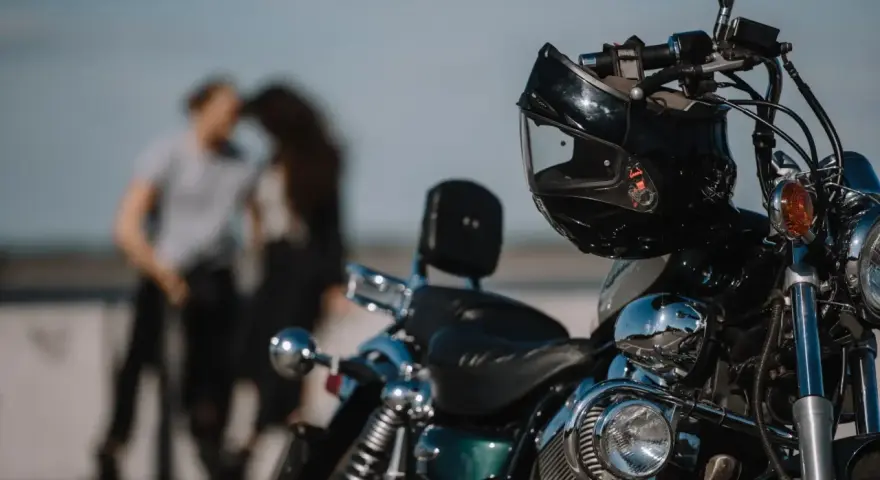 Motocykl z kaskiem na kierownicy, w tle para w czułym uścisku. Idealny dzień na wspólną podróż 4t.