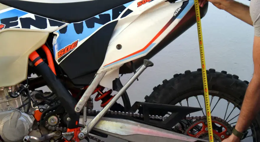 Mierzenie preload w amortyzatorze motocykla KTM 500 EXC. Dłoń trzyma miarkę przy tylnym kole.