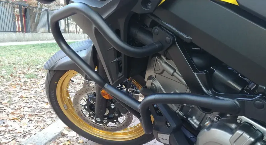 Żółty motocykl z czarnymi gmolami chroniącymi silnik i osłony. Złota obręcz koła i tarcza hamulcowa.