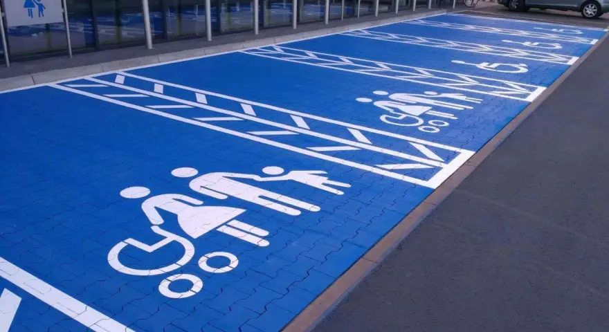 Niebieski parking z białymi symbolami osób na wózkach inwalidzkich i rodzin. Znak P19 informuje o przeznaczeniu miejsc.