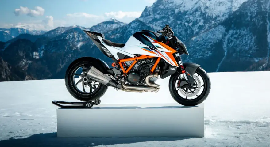Pomarańczowo-biały KTM Super Duke na śnieżnym tle z górami w tle.