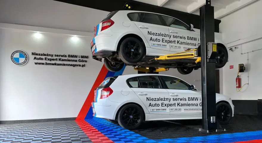 Dwa białe BMW, jedno na podnośniku, w serwisie Auto Expert. W tle logo BMW.