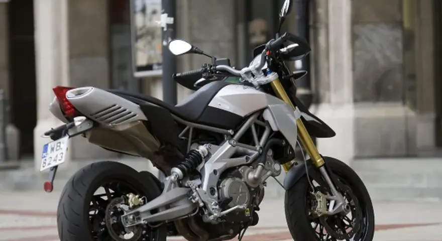 Srebrno-czarny motocykl Aprilia Dorsoduro 750 z żółtymi amortyzatorami, gotowy do jazdy po miejskich ulicach.