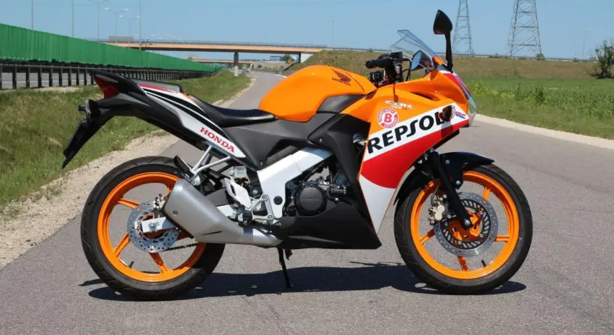 Pomarańczowy motocykl Honda CBR 125 Repsol na drodze. Warto sprawdzić honda cbr 125 dane techniczne przed zakupem.