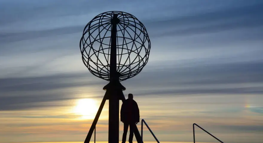 Sylwetka człowieka przy globusie na Nordkapp podczas zachodu słońca.