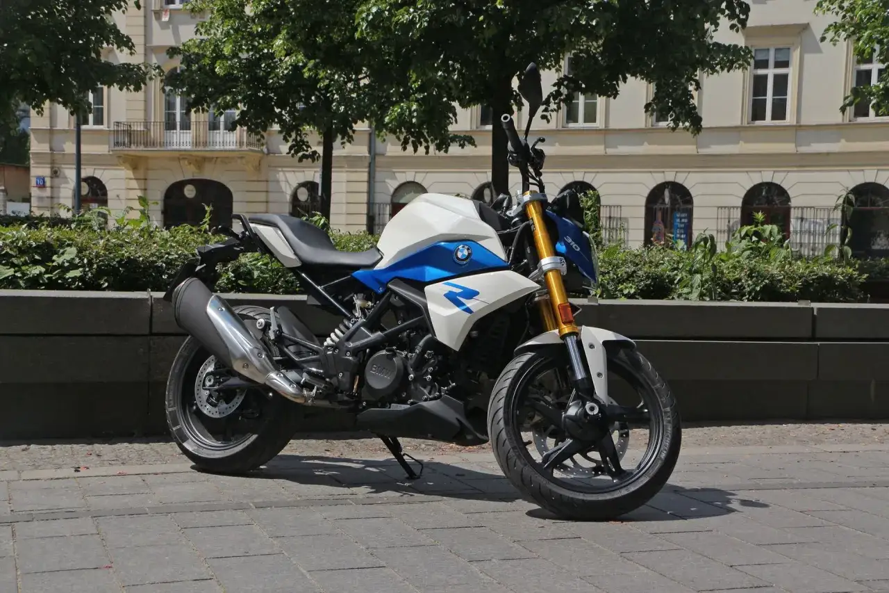 Biało-niebieski motocykl BMW G 310 R stoi na chodniku przed kamienicą.