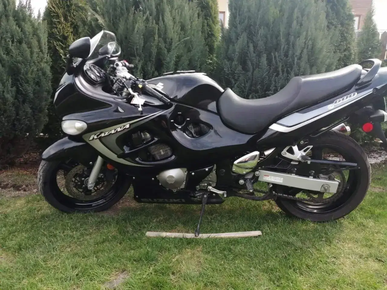 Czarny motocykl Suzuki GSXF 600 Katana stoi na trawie, otoczony zielonymi drzewami.