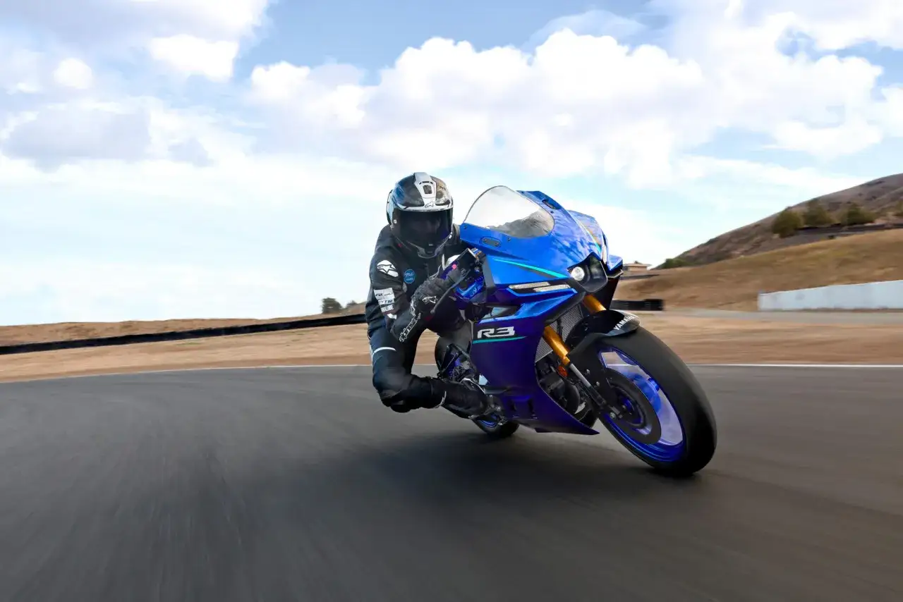 Motocyklista w kasku i kombinezonie pochyla się na torze na niebieskim motocyklu Yamaha R3. Poznaj yamaha r3 dane techniczne.