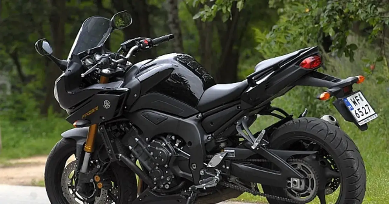 Czarny motocykl Yamaha Fazer 800 z przyciemnianą szybą, zaparkowany na tle zieleni.
