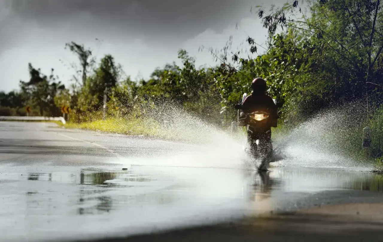 Motocyklista na mokrej drodze, tworząc fontannę wody. Niebezpieczny aquaplaning na zakręcie.
