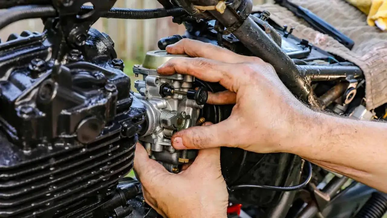 Dłonie mechanika regulują gaźnik motocykla, kluczowy element odpowiedzialny za symbol ssania paliwa i powietrza do silnika.