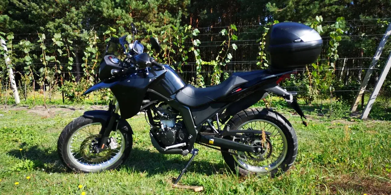 Czarny motocykl Derbi Terra 125 z kufrem na bagaż, zaparkowany na trawie wśród zieleni i winorośli.