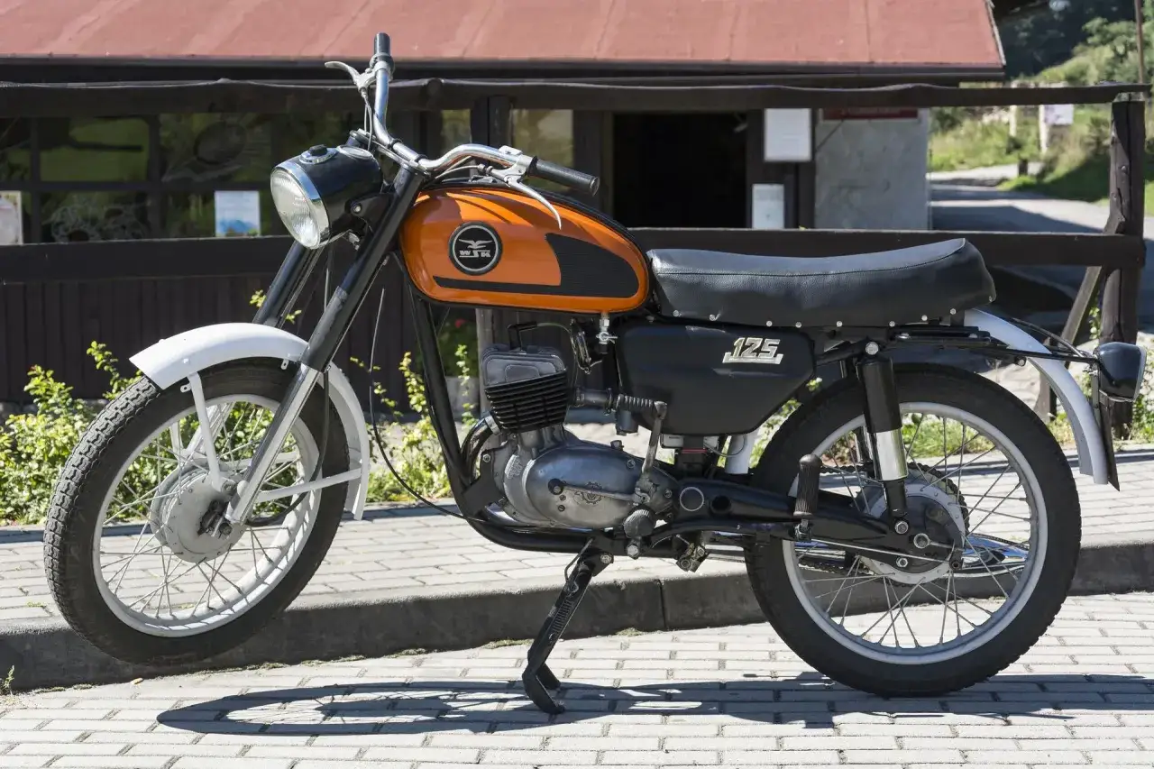 Klasyczny motocykl WSK 125, z charakterystycznym pomarańczowym bakiem i silnikiem, gotowy do jazdy.