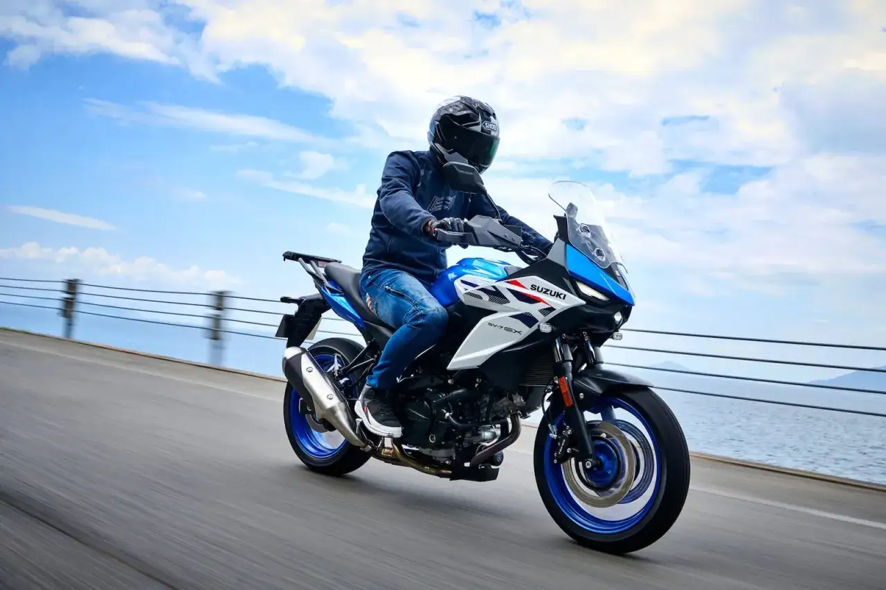 Motocyklista w kasku i jeansach pędzi niebiesko-białym Suzuki SV650X. W tle błękitne niebo i morze. Idealny dzień na blokowanie motocykla na A2.