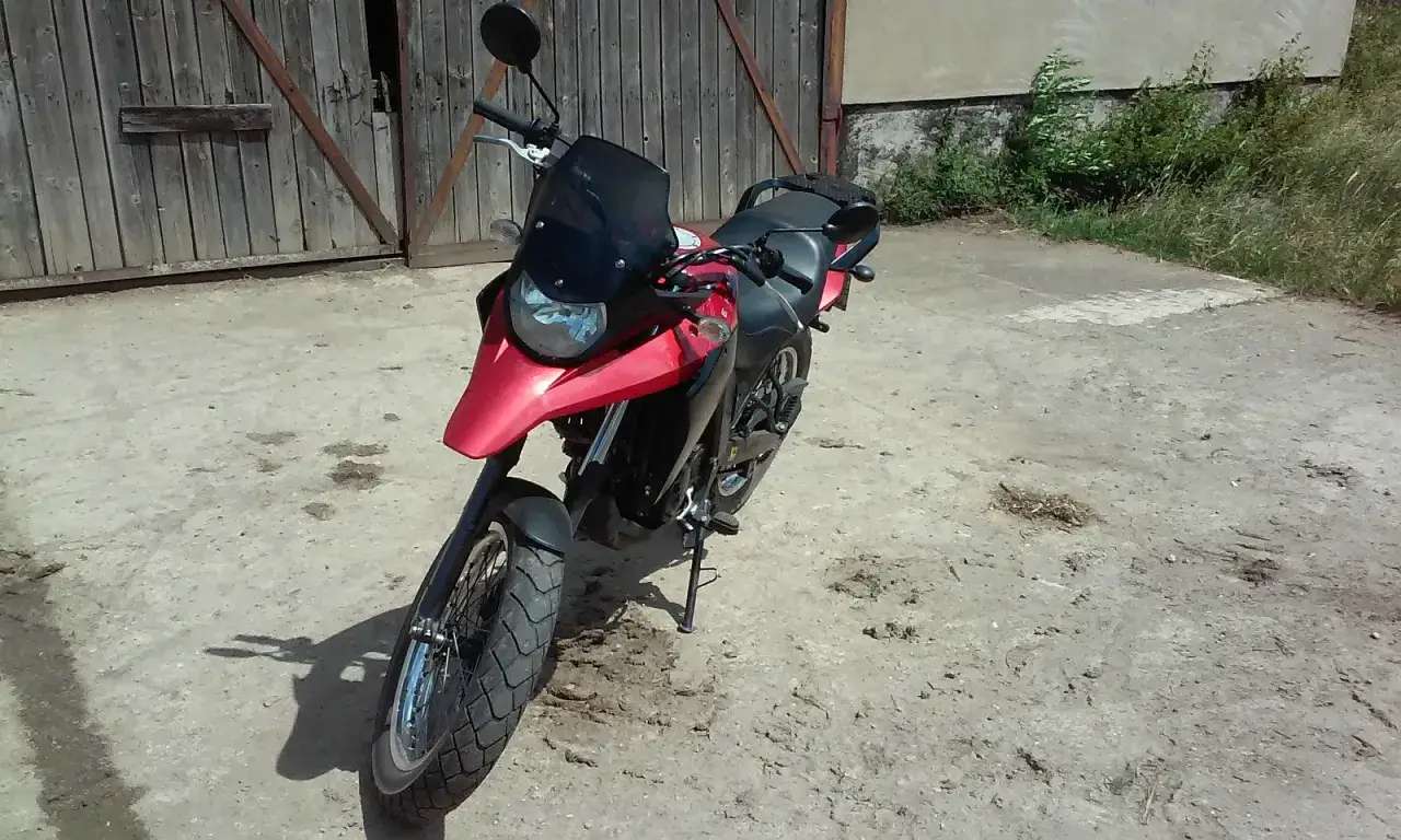 Czerwony motocykl Derbi Terra 125 stoi przed drewnianą stodołą.