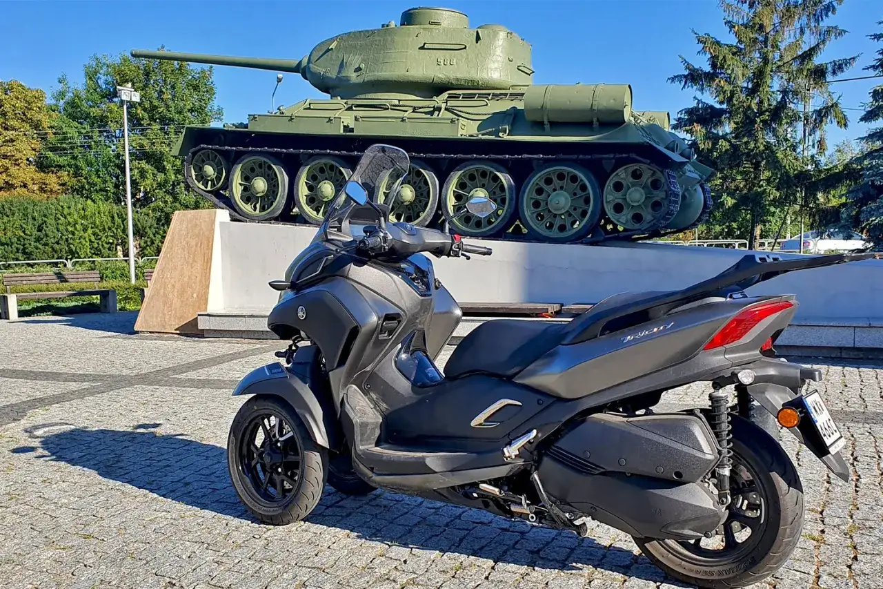 Szary skuter Yamaha Tricity 300 na tle zabytkowego czołgu. Zastanawiam się, jaka jest jego yamaha tricity 300 prędkość maksymalna.