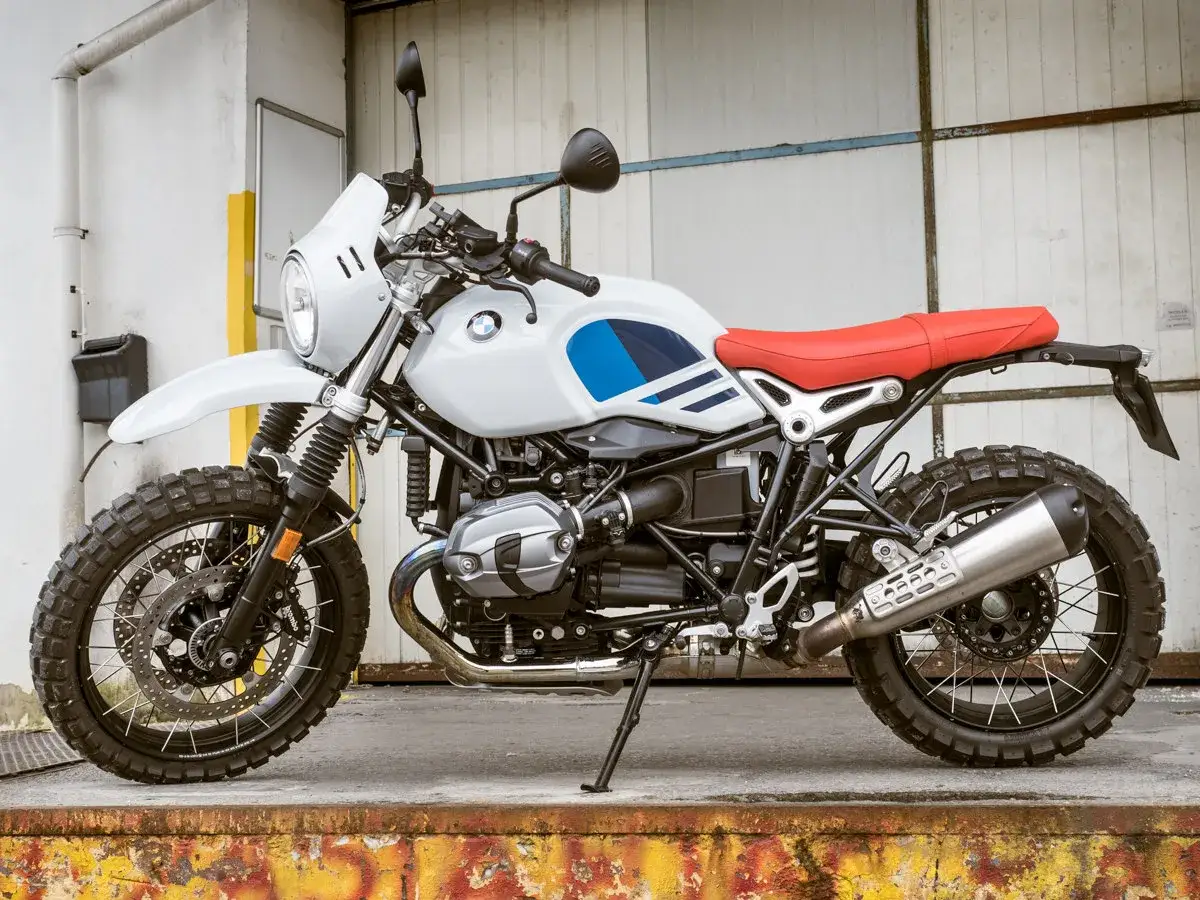 Biały motocykl BMW R nine T z czerwoną kanapą i niebieskimi akcentami na baku, gotowy na przygodę.