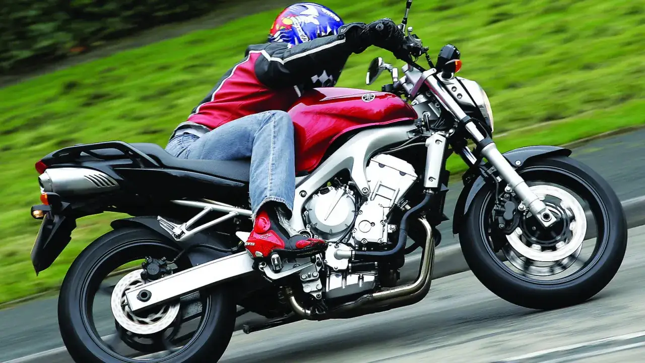 Motocyklista w kasku i czerwonej kurtce pędzi na błyszczącym, czerwonym motocyklu Yamaha FZ6.