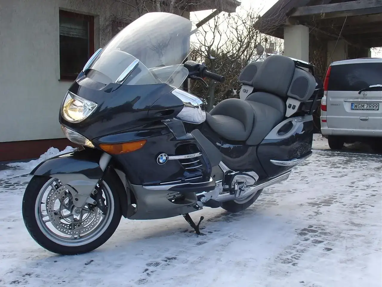 Ciemnogranatowy BMW K1200LT z dużym, przezroczystym wiatrochronem, zaparkowany na zaśnieżonym podjeździe.