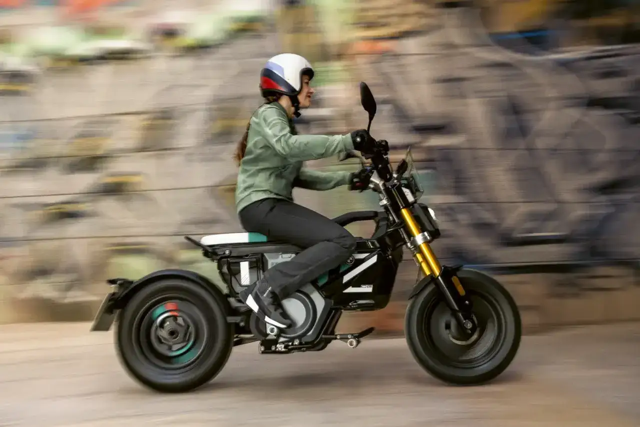 Kobieta w kasku jedzie na elektrycznym motocyklu BMW CE02. Tło jest rozmyte, sugerując ruch.