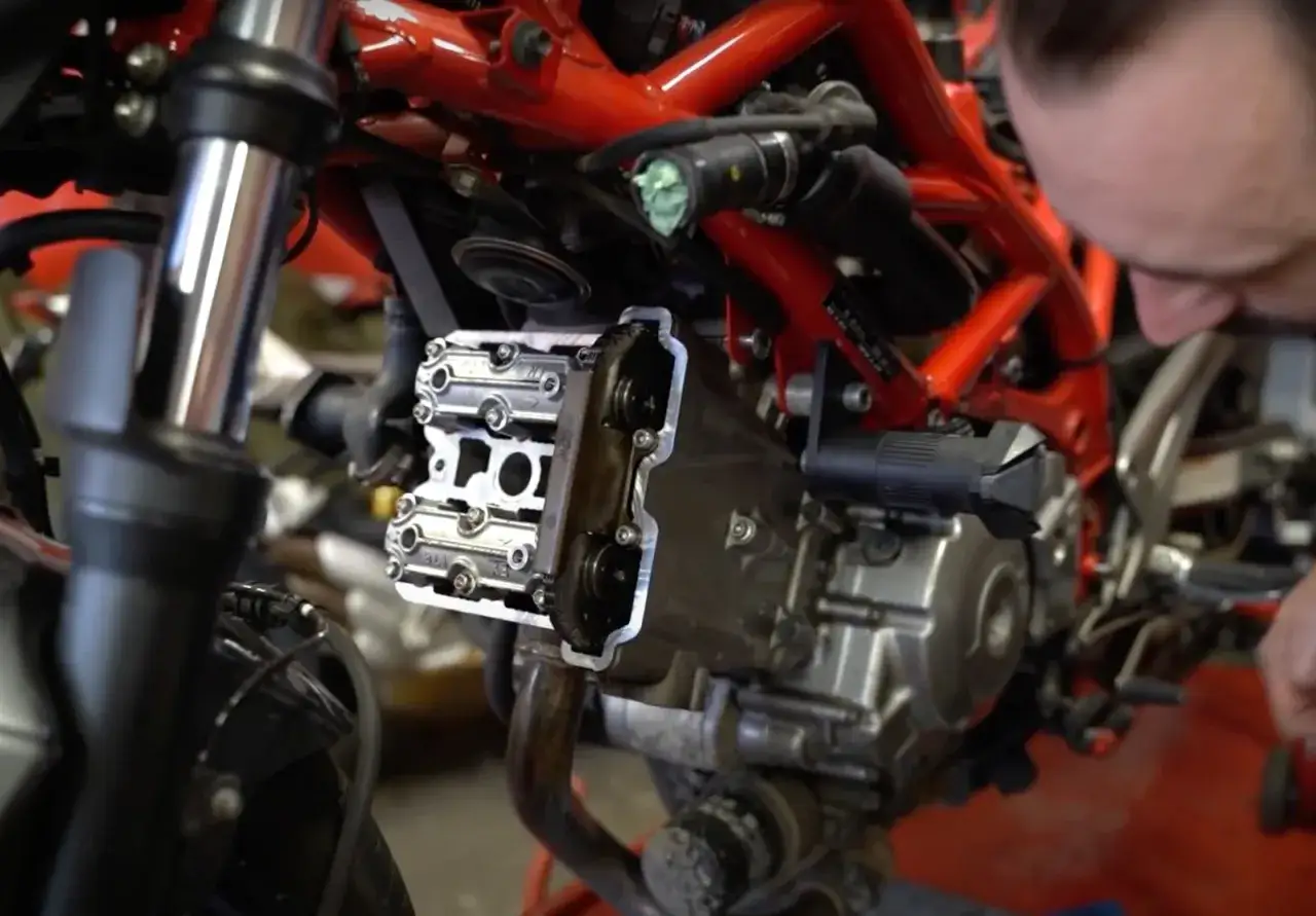 Mechanik pracuje nad silnikiem motocykla z podwójnym wałkiem rozrządu (dohc). Widoczne są zawory i elementy układu rozrządu.