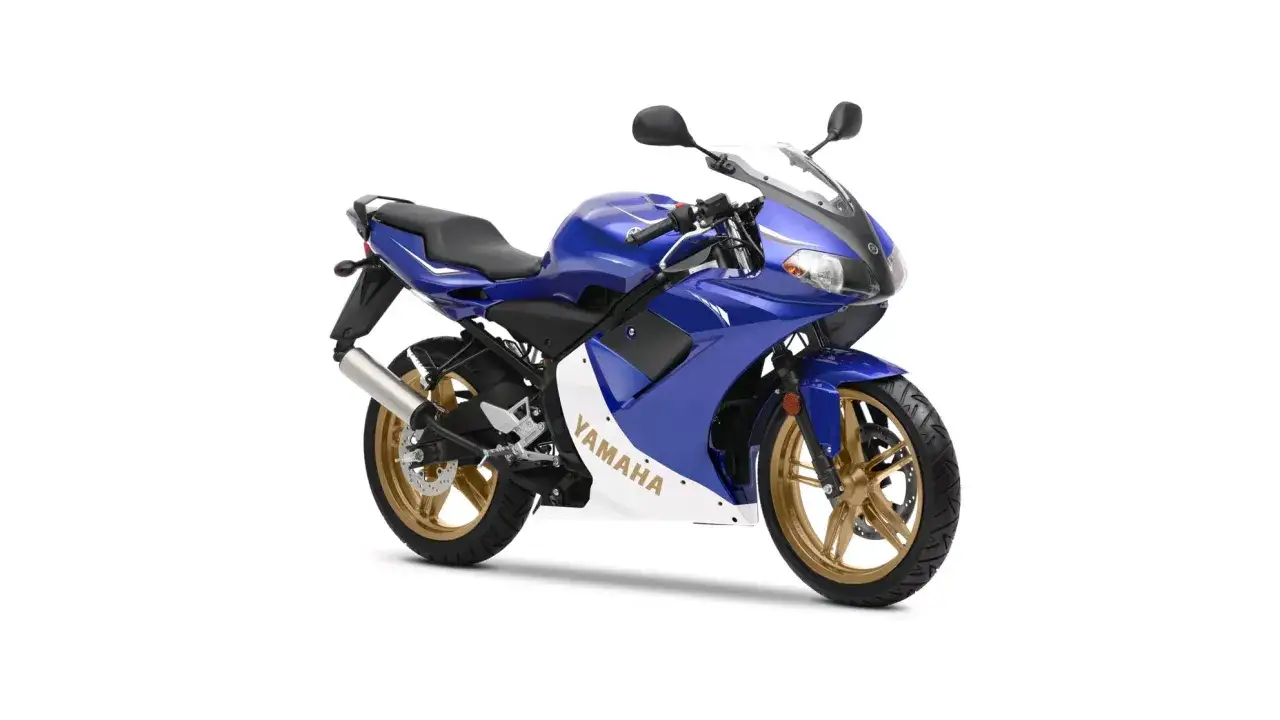 Niebieski motocykl Yamaha TZR 50 z białym pasem i złotymi felgami, gotowy do osiągnięcia v-max.