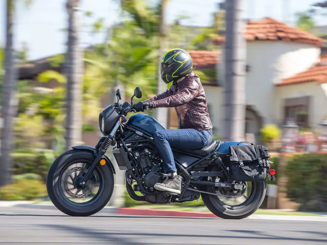 Kobieta na ciemnoniebieskim motocyklu Honda Rebel, w skórzanej kurtce i kasku, przemierza słoneczną ulicę. Czy to ten chopper jest najmniej awaryjny?