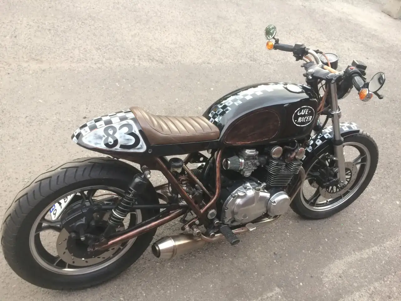 Customowy Suzuki GS 650 w stylu cafe racer, z brązową tapicerką i czarno-białymi szachownicami.