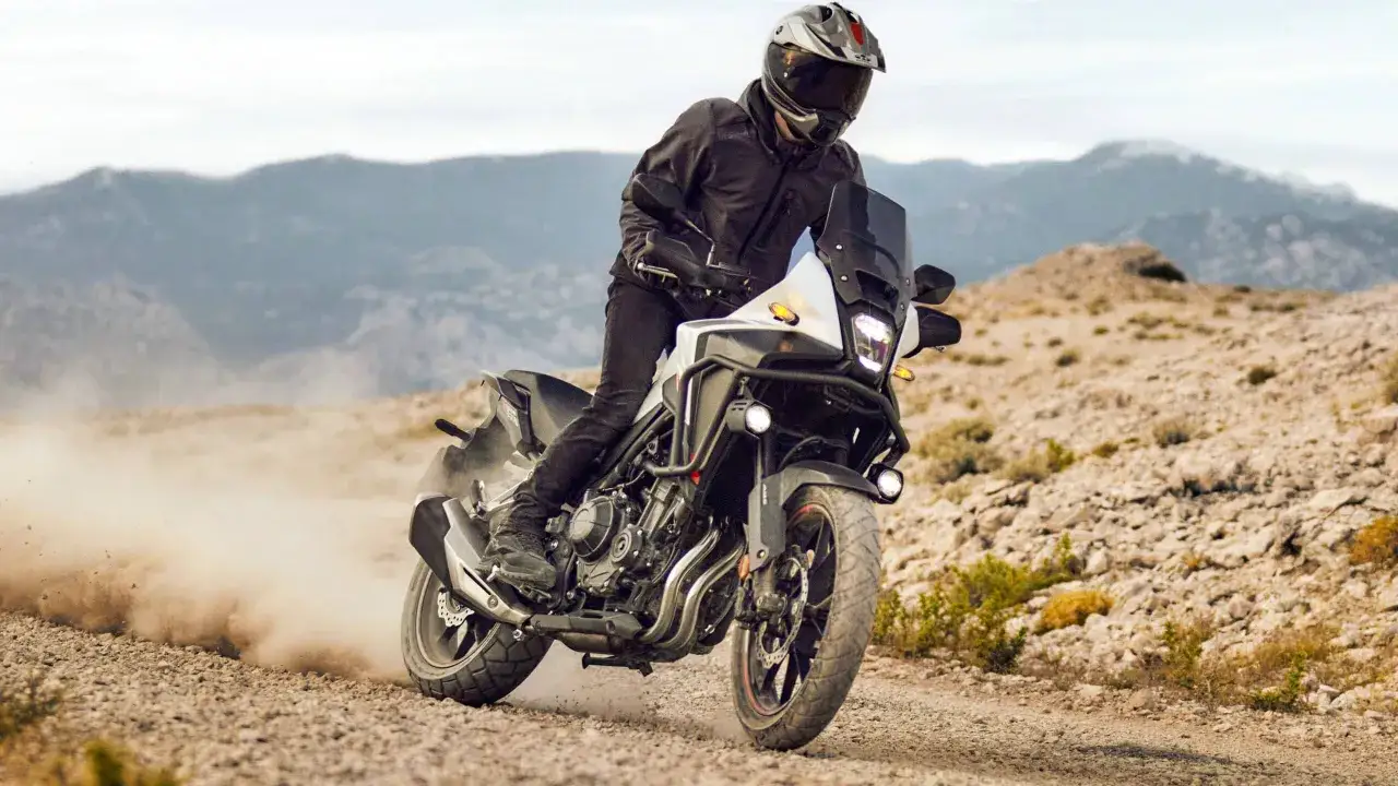 Motocyklista na Honda NX 500 przemierza pustynny teren, wzbijając tumany kurzu.