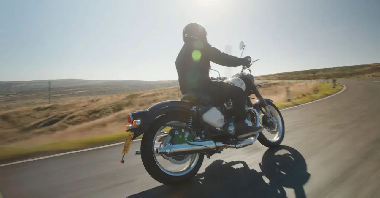 Motocyklista na Royal Enfield Classic 650 przemierza malowniczą, pagórkowatą trasę w słoneczny dzień.