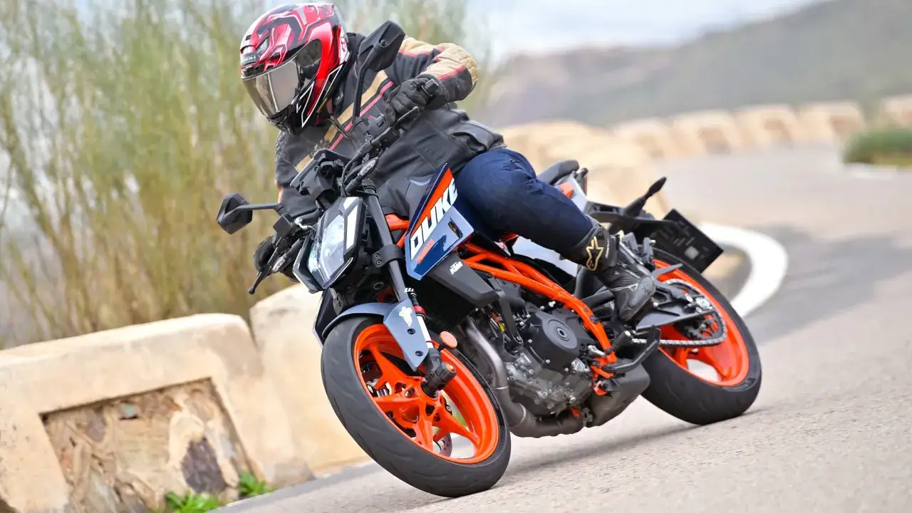 Motocyklista w kasku ściga się na KTM Duke 390, osiągając maksymalną prędkość na krętej drodze.
