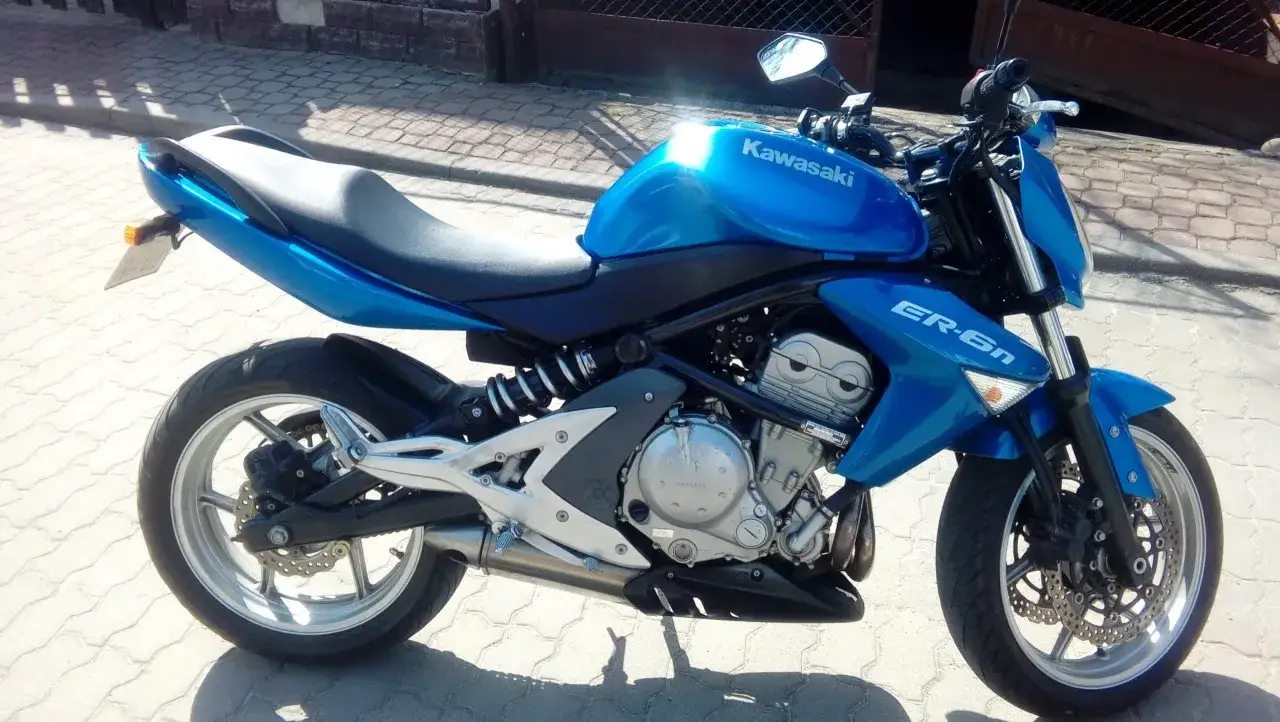 Błękitny motocykl Kawasaki ER-6n z widocznym silnikiem i siedzeniem, zaparkowany na chodniku.
