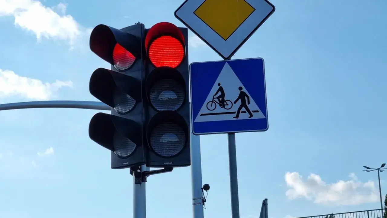 Czerwone światło na sygnalizatorze. Znak informuje, że rowerzysta ma pierwszeństwo na przejeździe rowerowym.