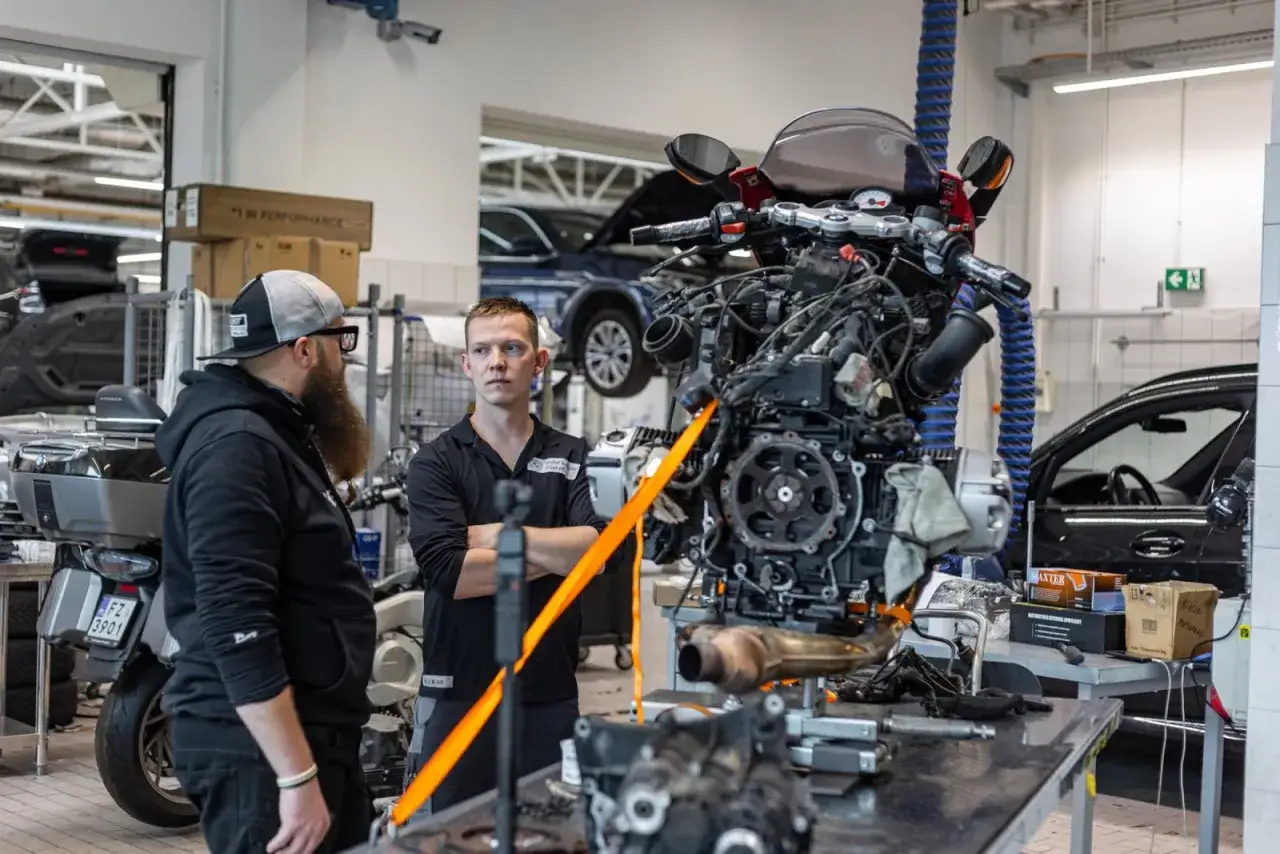 Mechanicy omawiają wymianę sprzęgła w motocyklu. Silnik jest wyjęty i przygotowany do pracy.