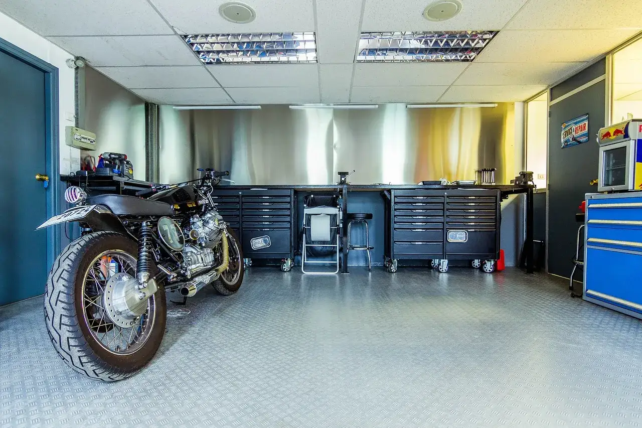 Warsztat z motocyklem i 2 rzędami szafek narzędziowych.