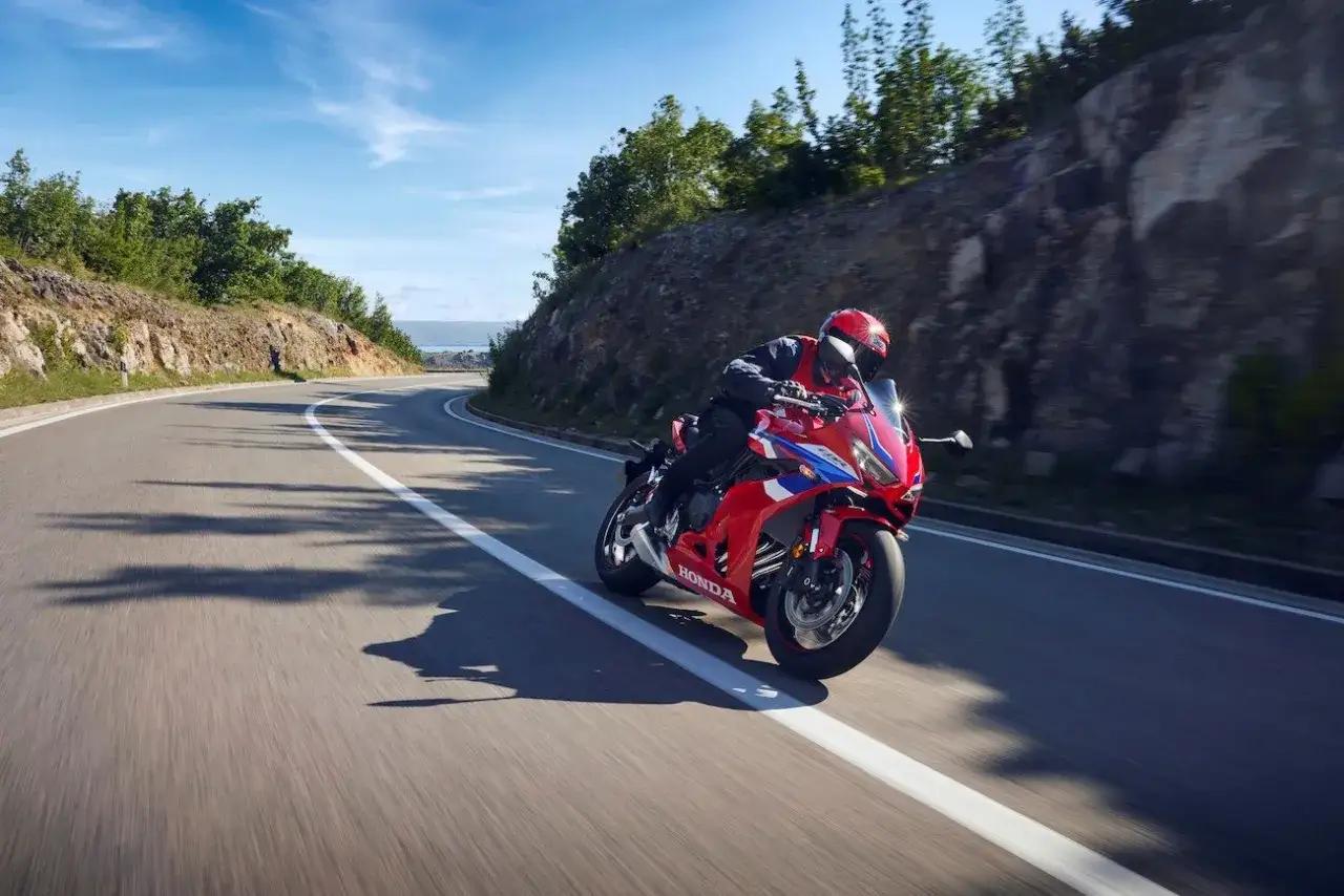 Motocyklista w kasku śmiga na czerwonym motocyklu Honda CBR650R po krętej drodze z widokiem na morze.