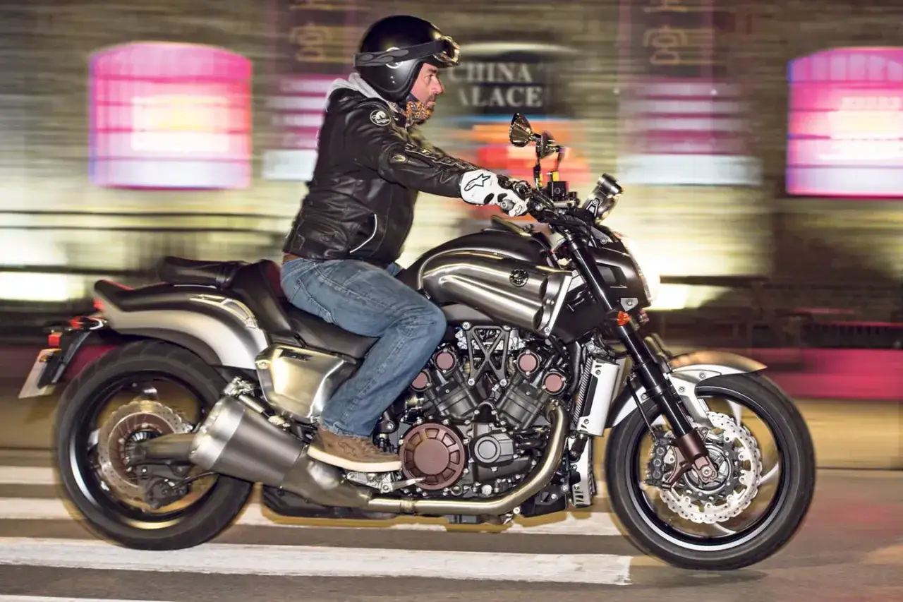 Mężczyzna w kasku i skórzanej kurtce jedzie nocą na motocyklu Yamaha V-Max 1700.