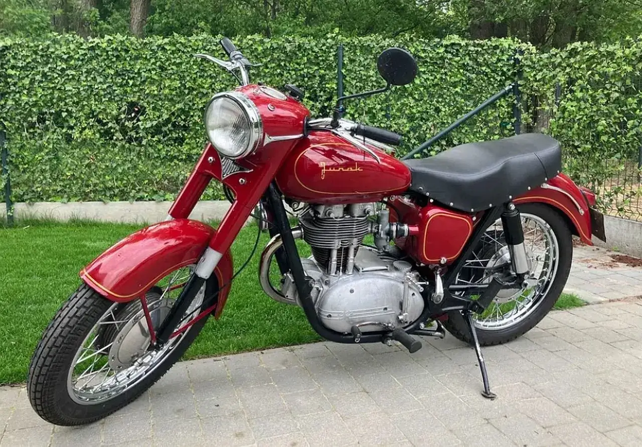 Czerwony Junak, klasyk polskiej motoryzacji, lśni na tle zielonego żywopłotu. To właśnie co to wsk, symbol wolności i przygody.