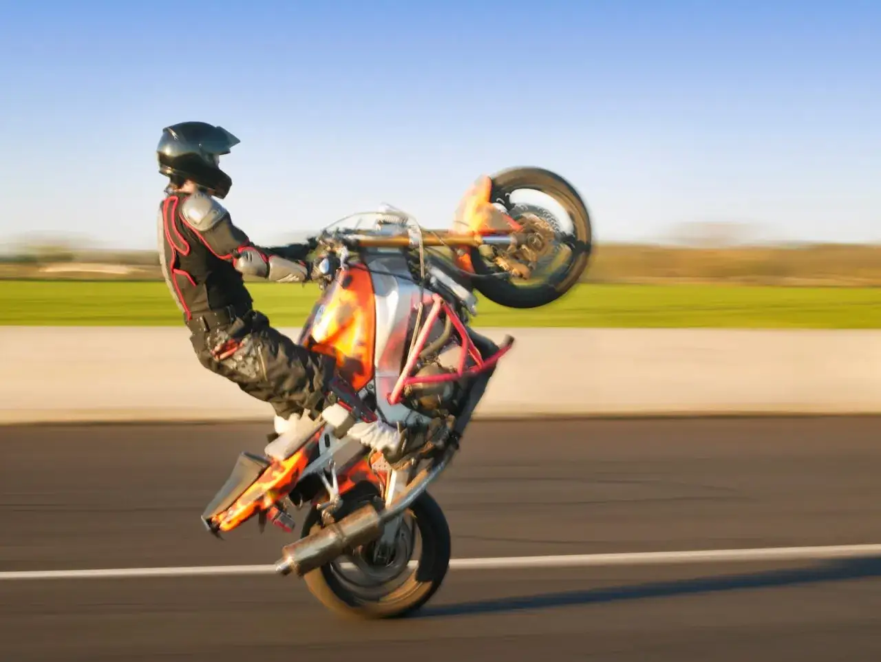 Motocyklista w kasku i kombinezonie wykonuje jazdę na jednym kole. Ryzykowna zabawa, za którą grozi mandat.