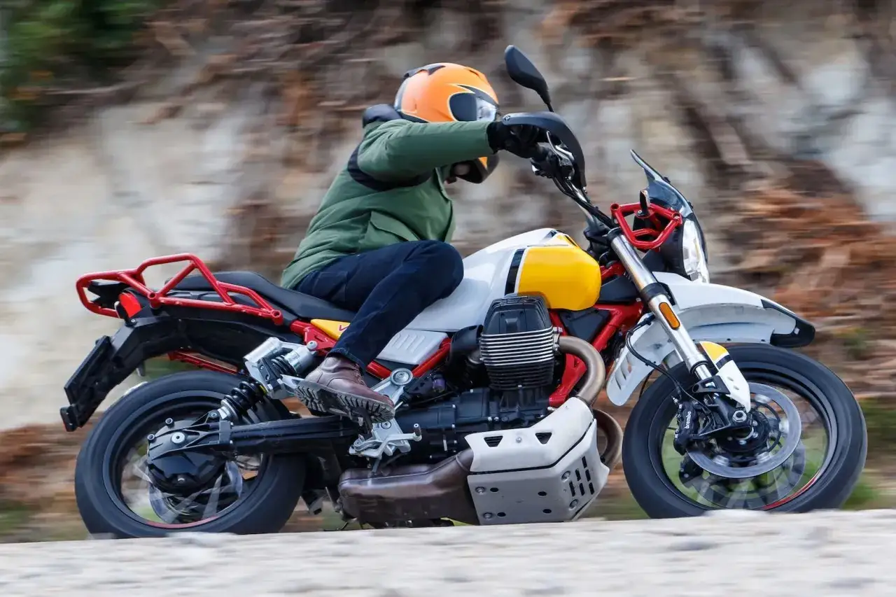 Motocyklista na motocyklu Moto Guzzi V85 TT przemierza malowniczą, kamienistą drogę.