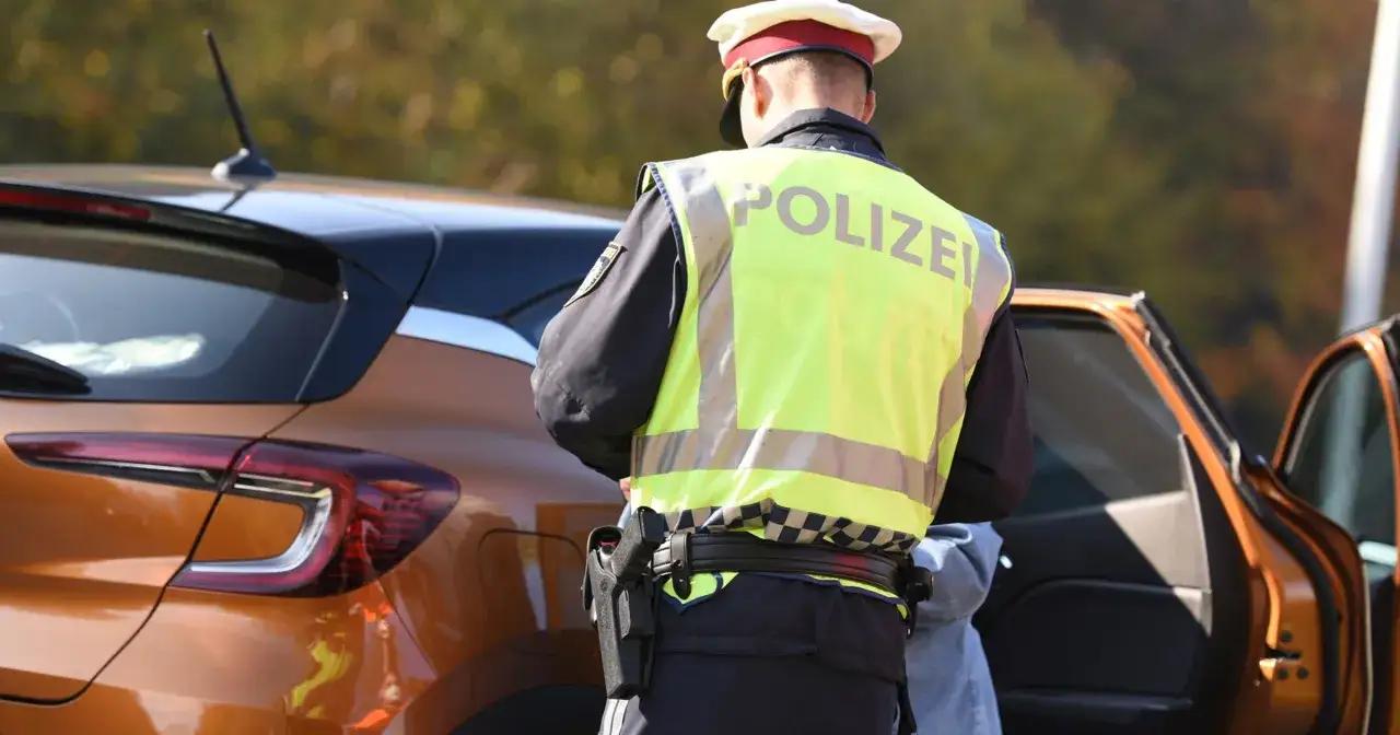 Austriacki policjant w kamizelce odblaskowej przy pomarańczowym samochodzie. Może to oznaczać kontrolę drogową lub mandaty w Austrii.