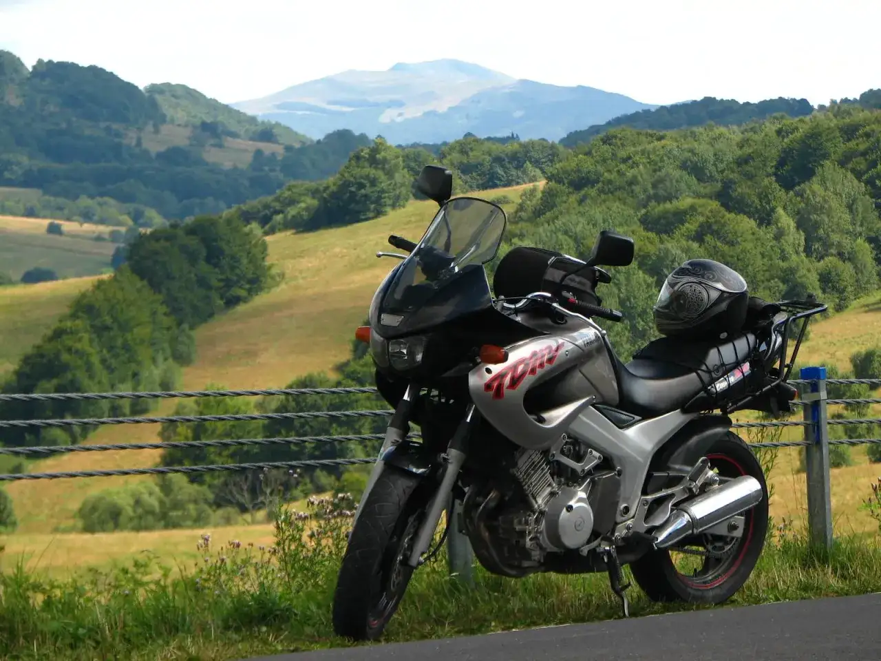 Yamaha TDM 850 zaparkowana na tle malowniczych, zielonych wzgórz. Kask motocyklowy spoczywa na siedzeniu.
