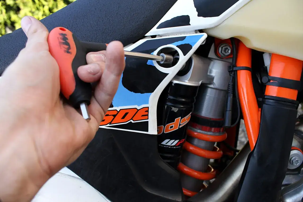 Ręka dokręca śrubę kluczem imbusowym, regulując preload w amortyzatorze motocykla KTM.