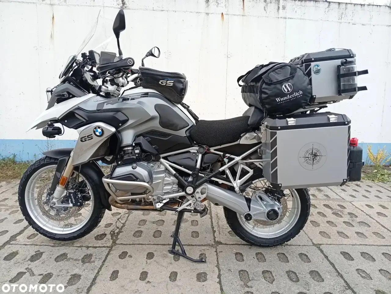 Srebrny BMW R 1200 GS z kuframi i torbami, gotowy na wyprawę. Choć jego wady są dyskusyjne, to wszechstronność jest jego mocną stroną.