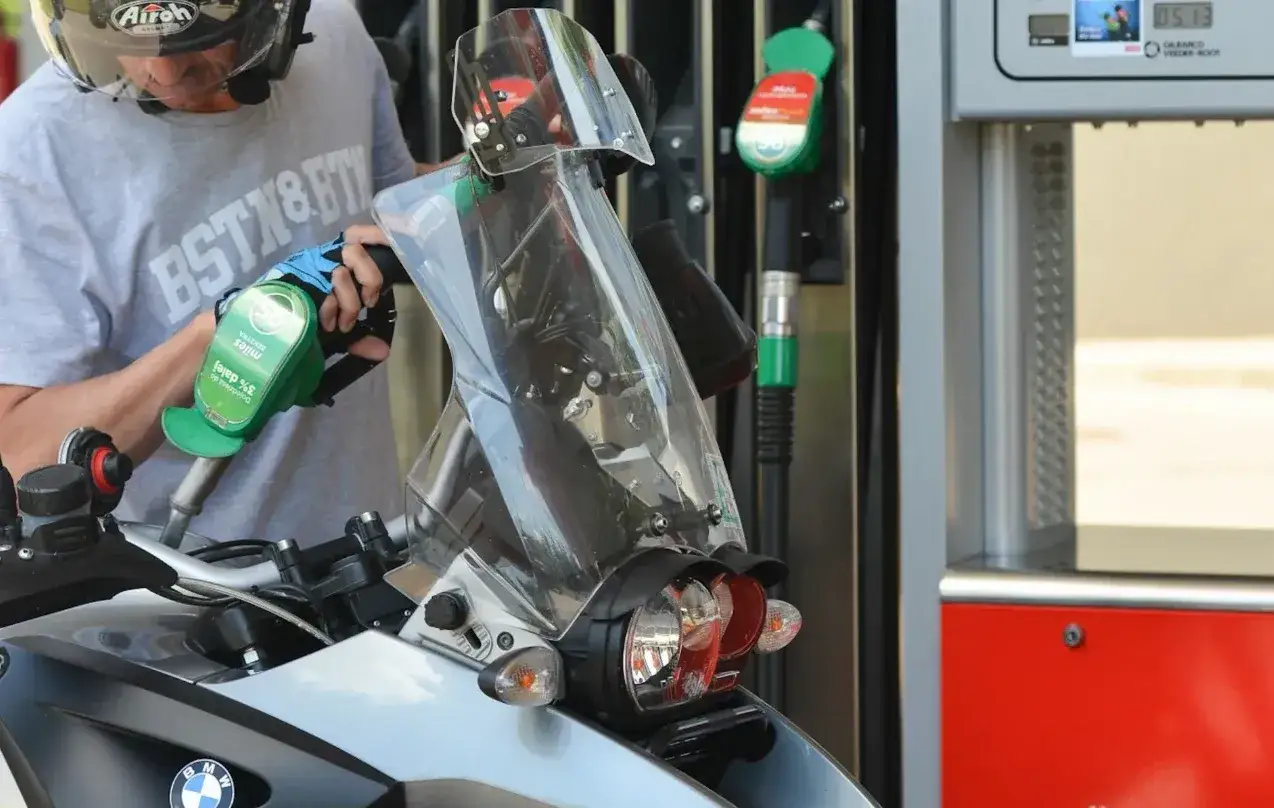 Motocyklista tankuje paliwo 100. Zielony pistolet z dystrybutora wlewa benzynę do baku.